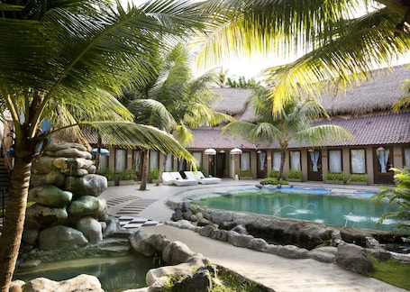 A resort with a pool, palm trees, and a thatched-roof building.