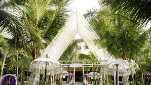 Um jardim tropical com um gazebo branco, palmeiras e uma estátua.