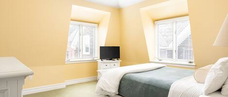Un dormitorio con dos ventanas, una cama, una mesita de noche y un televisor.