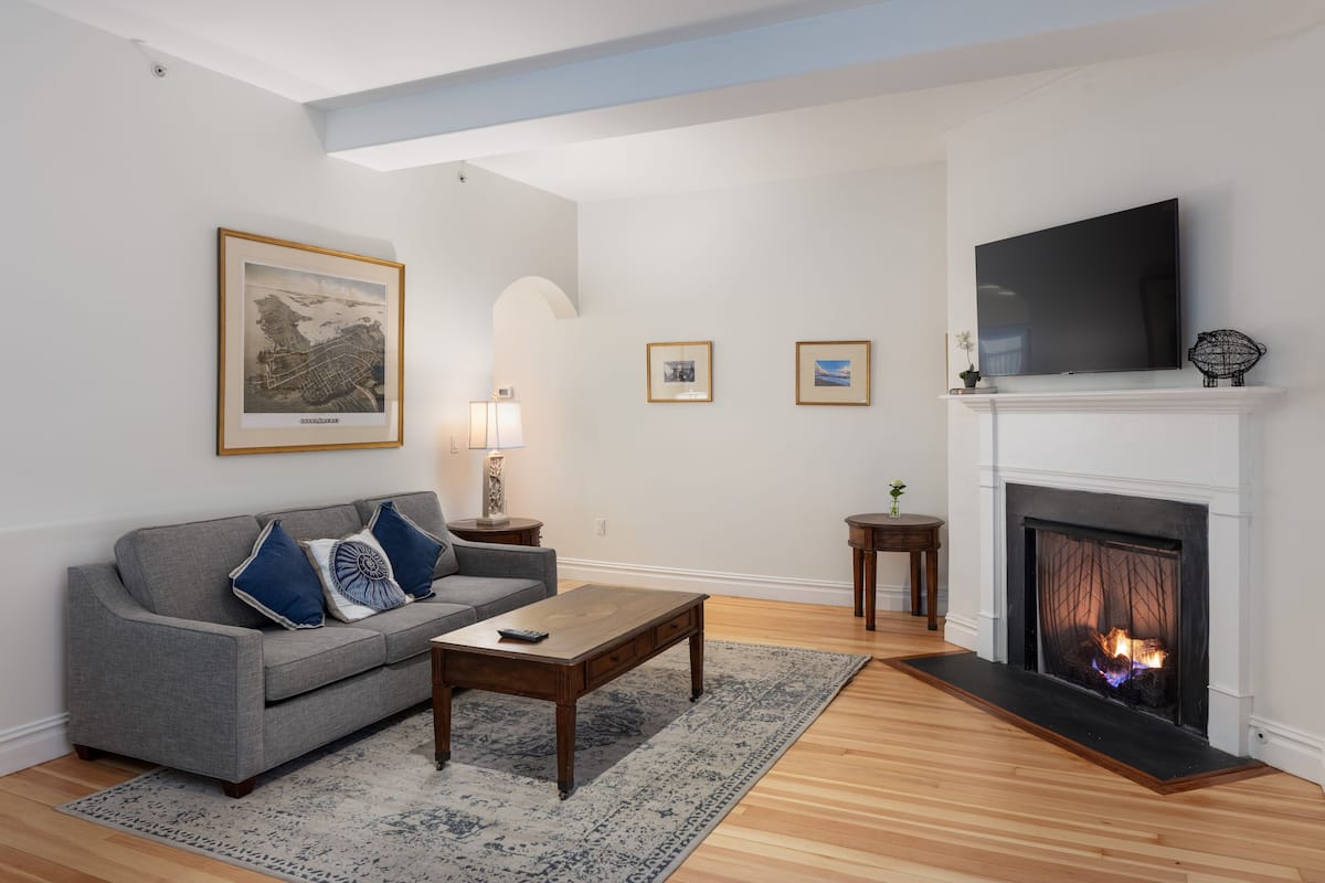 A living room with a fireplace, a sofa, a coffee table, and a TV mounted above the fireplace.