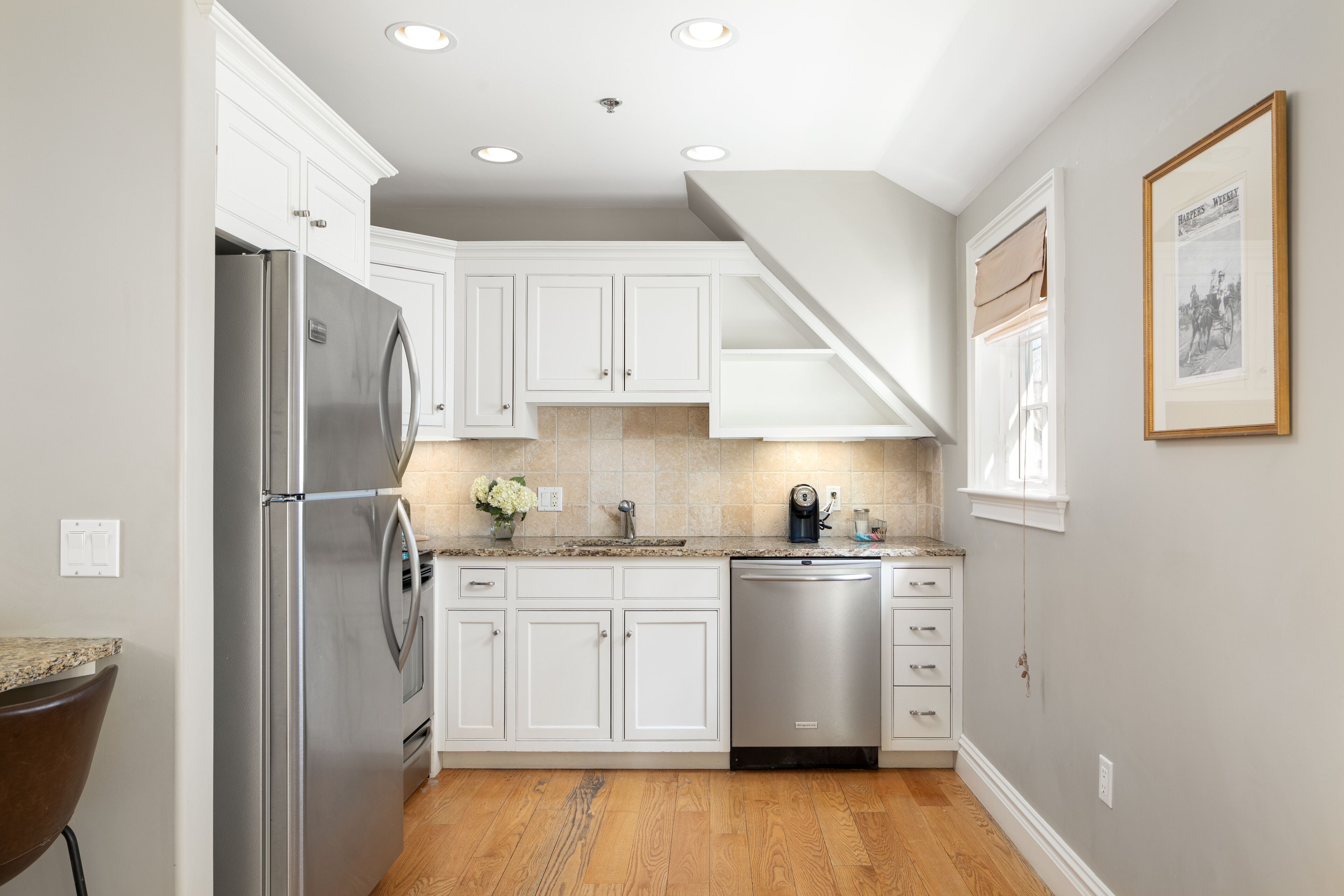 A modern kitchen with white cabinetry, stainless steel appliances, and a wooden floor.