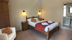 Un dormitorio con una cama individual, dos mesitas de noche, una tocador, una silla y un baño con lavabo y espejo.