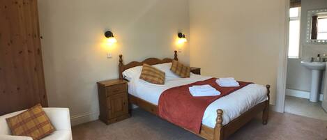 A bedroom with a single bed, two bedside tables, a nightstand, a chair, and a bathroom with a sink and mirror.