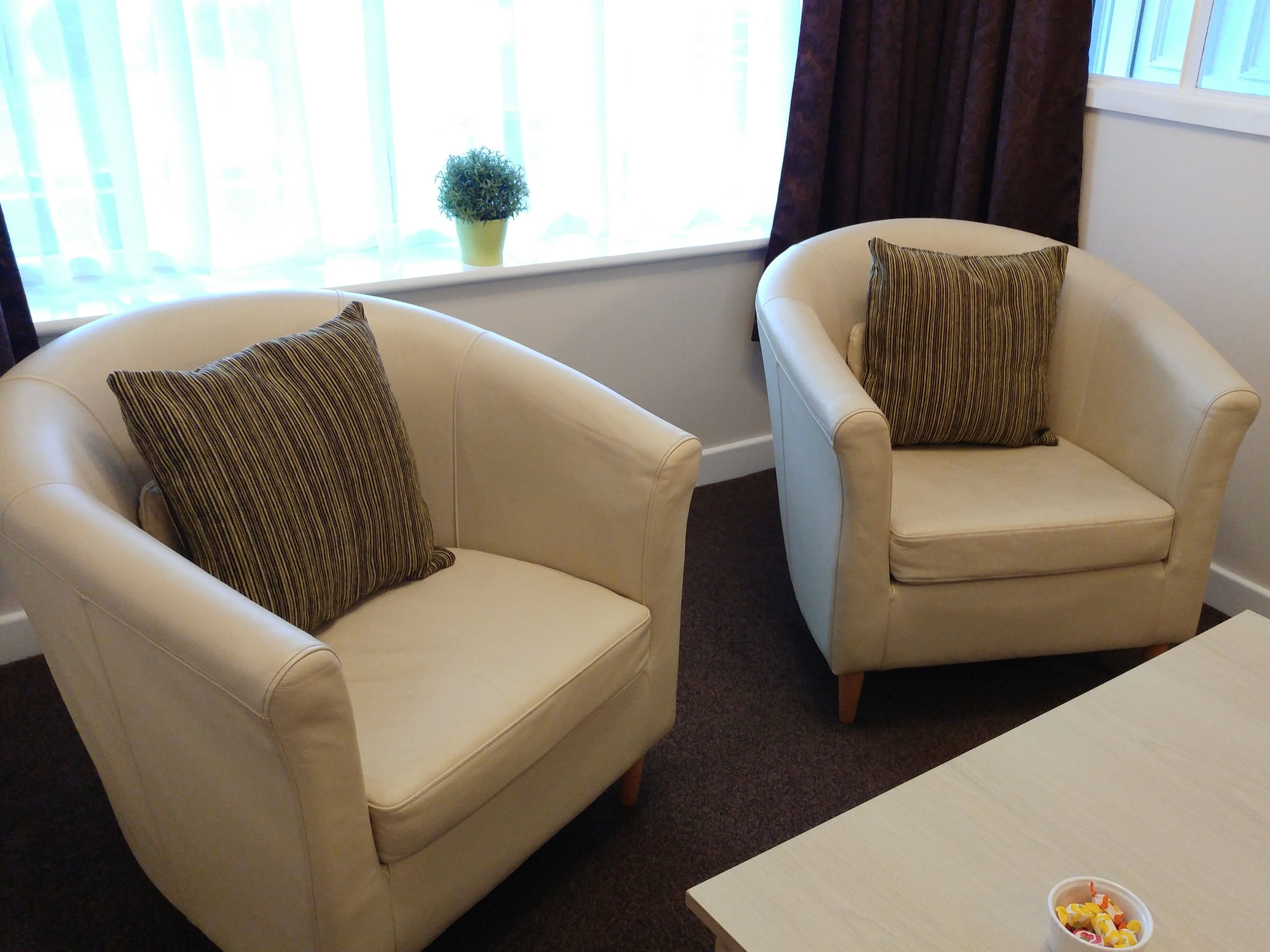 Two beige armchairs with striped pillows, a small potted plant, and a coffee table with a bowl of fruit.