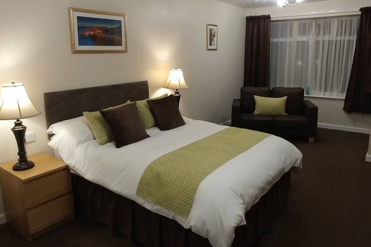 Une chambre d’hôtel avec un grand lit, deux lampes de chevet, un canapé et une fenêtre avec des rideaux.