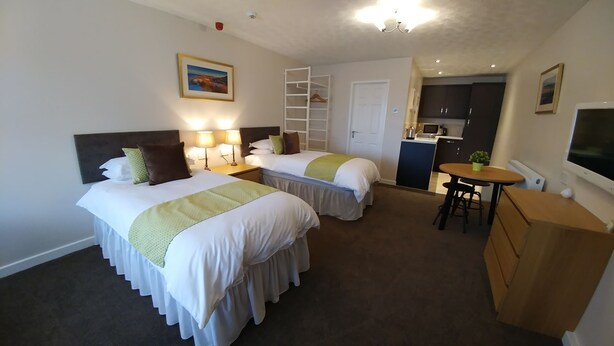 A hotel room with two beds, a kitchenette, a dining area, and a walk-in closet. - Swan Studios (Choppington)