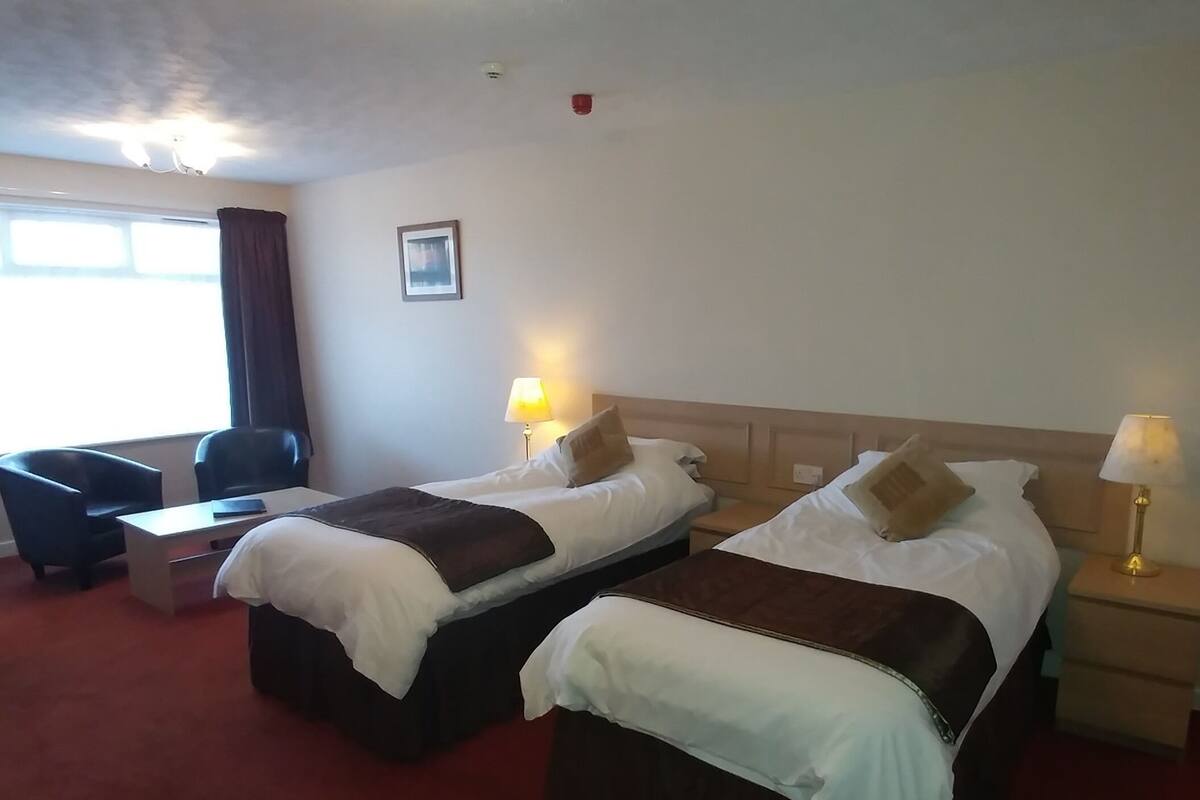 Une chambre d’hôtel avec deux lits, un bureau, une chaise et une fenêtre.