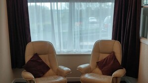 A room with two leather armchairs, a small table, and a window with curtains. - Swan Studios (Choppington)