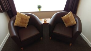 Two dark brown leather armchairs with matching cushions, positioned facing each other with a small wooden table between them. - Swan Studios (Choppington)