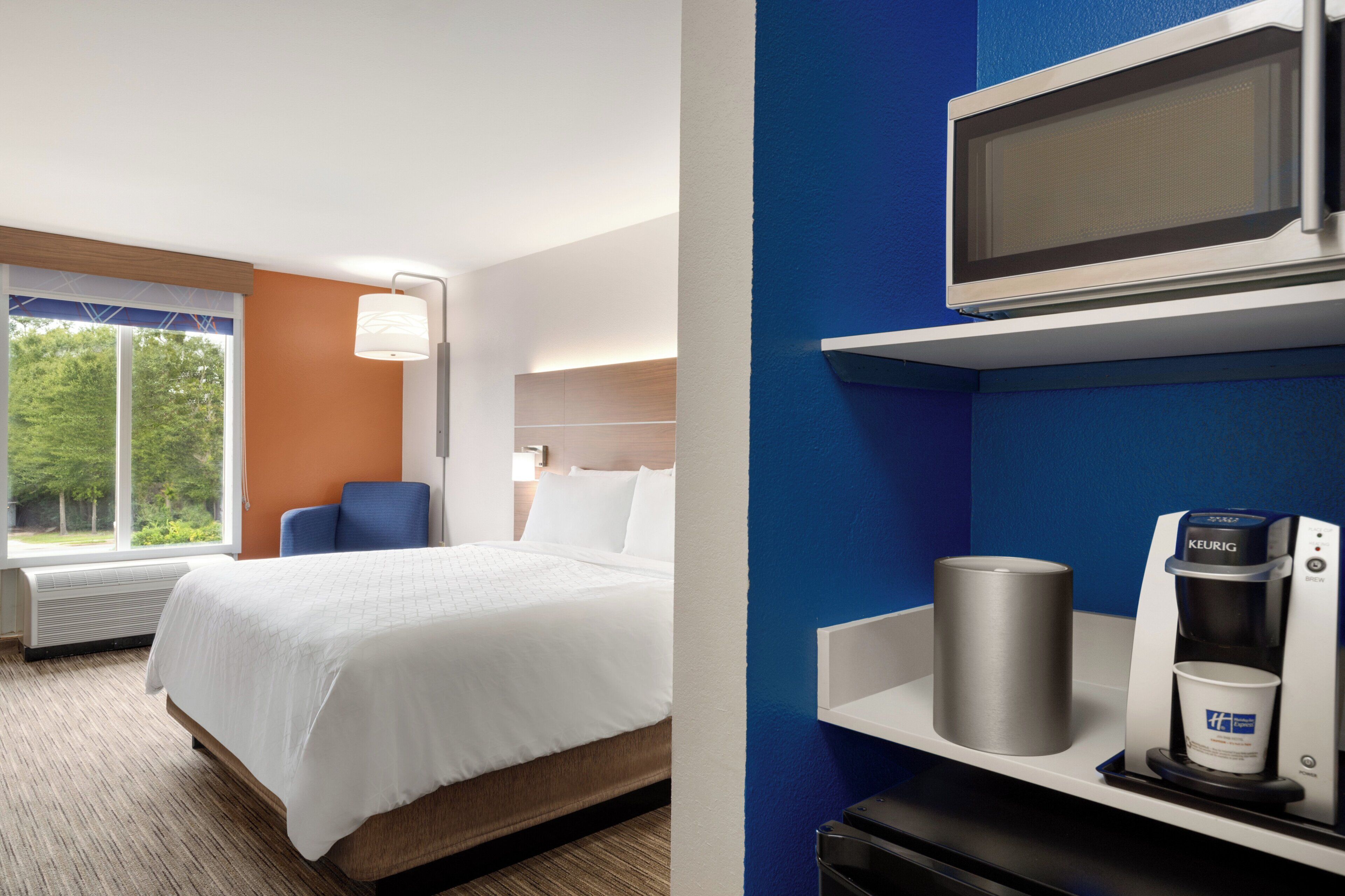 A hotel room with a bed, a chair, a window with a view of trees, and a coffee machine.