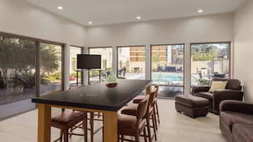 A modern living room with a dining area, large windows, and a view of a swimming pool.