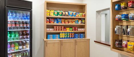 A vending machine with various drinks and snacks, a shelf with packaged snacks, and a display of coffee pods.