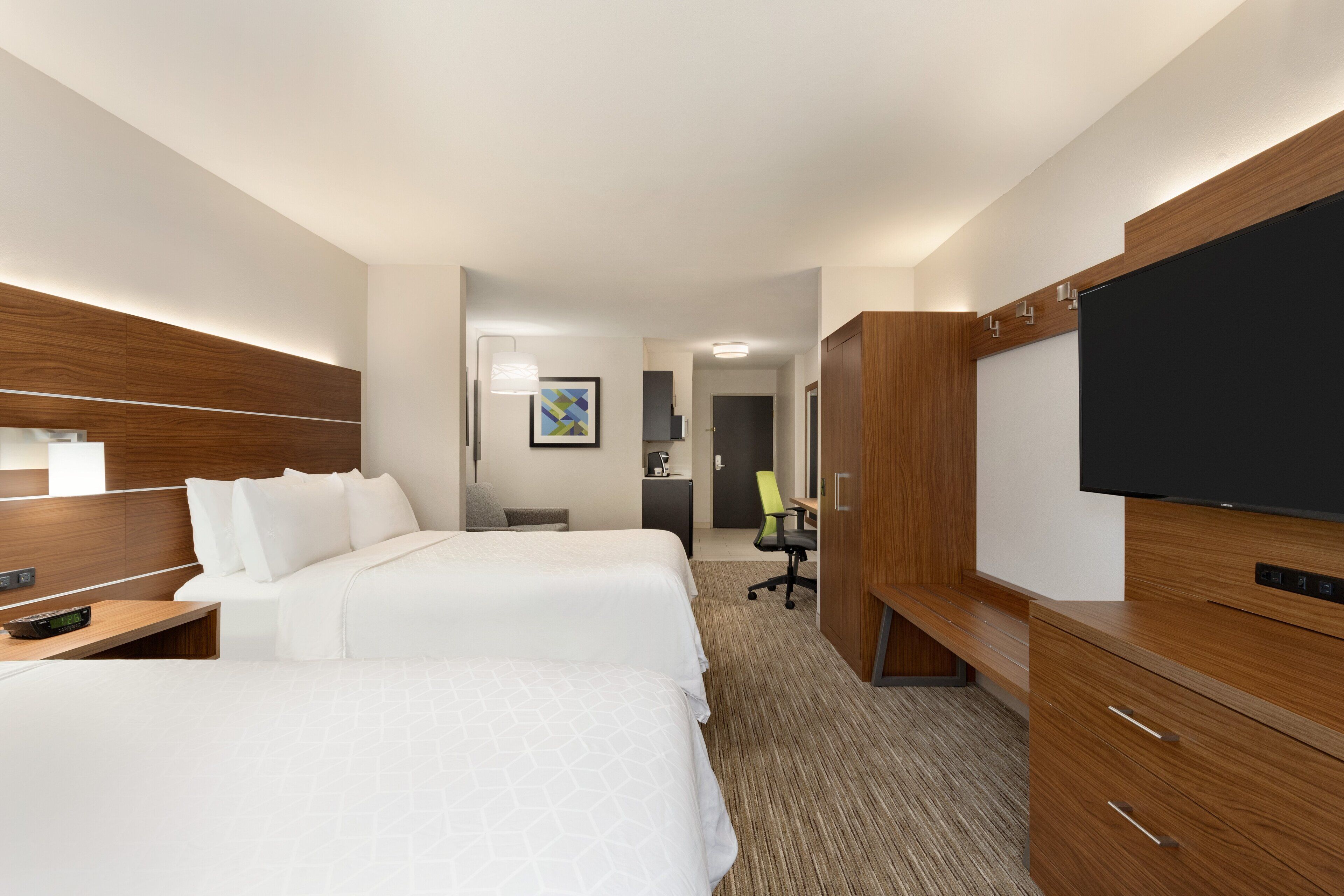 A hotel room with two beds, a TV, a desk with a lamp, and a wooden wardrobe.