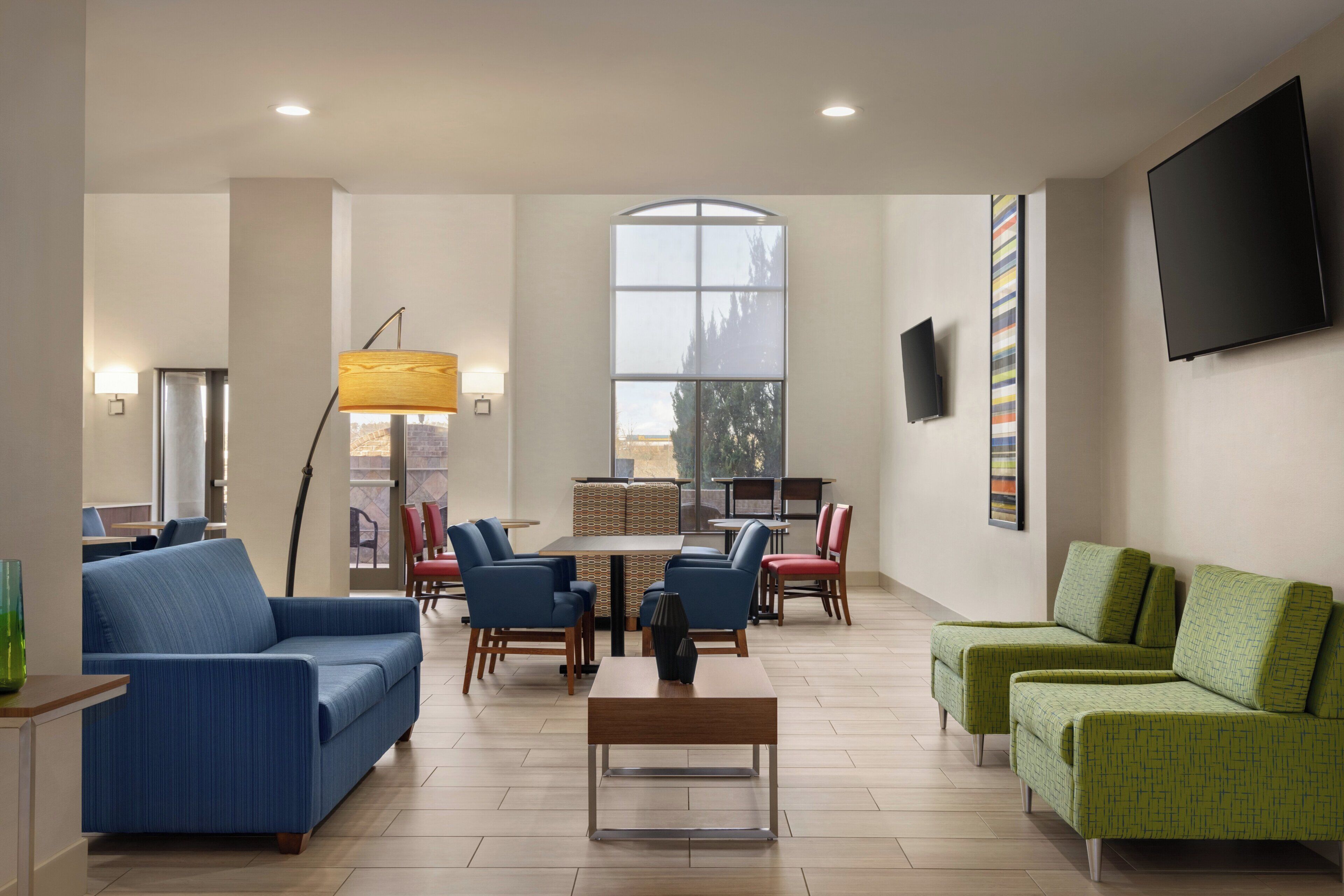 A spacious lounge area with seating arrangements, a large window, and a flat-screen TV mounted on the wall.