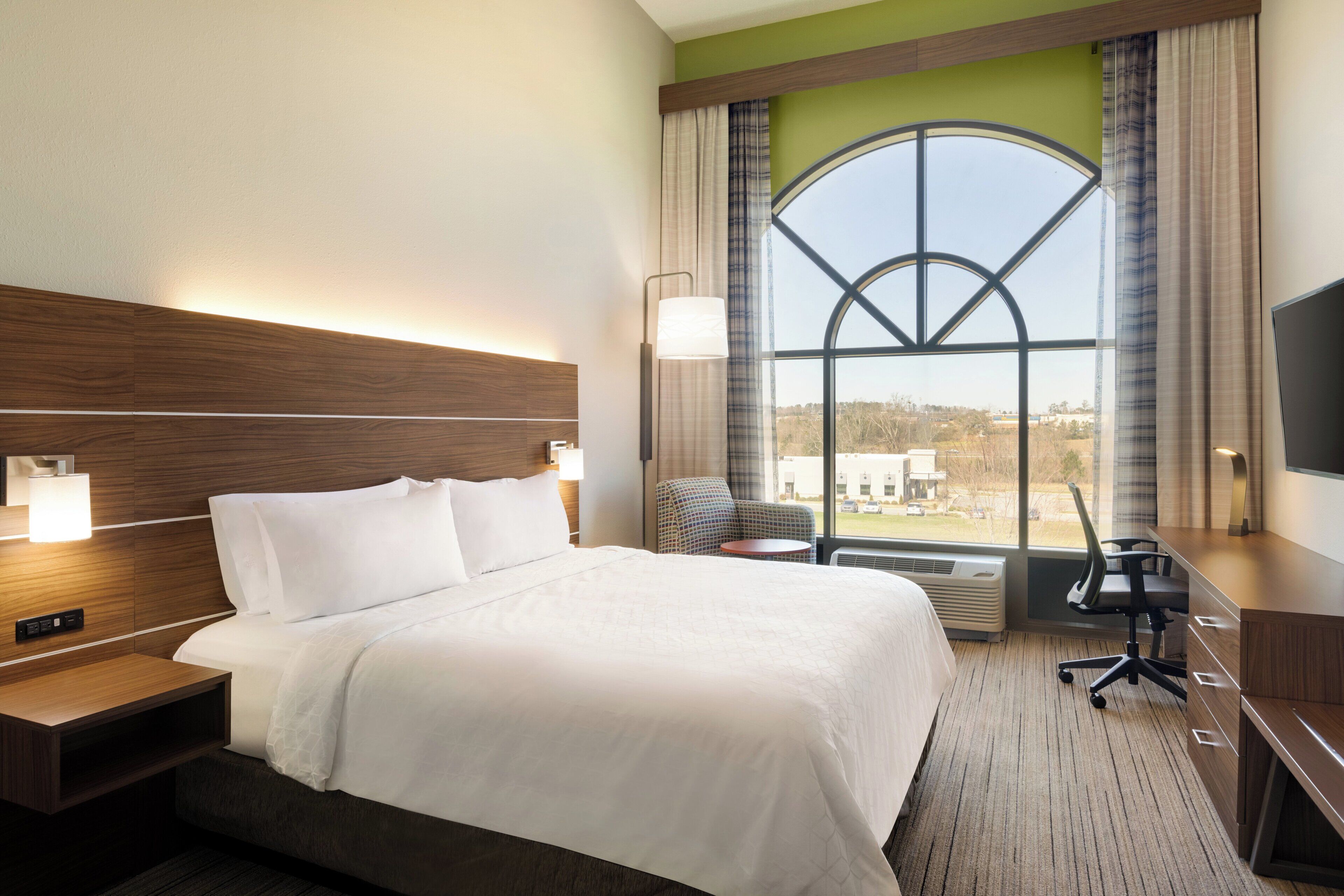 A hotel room with a large bed, a desk, a chair, a TV, and a window with a view of the outside.