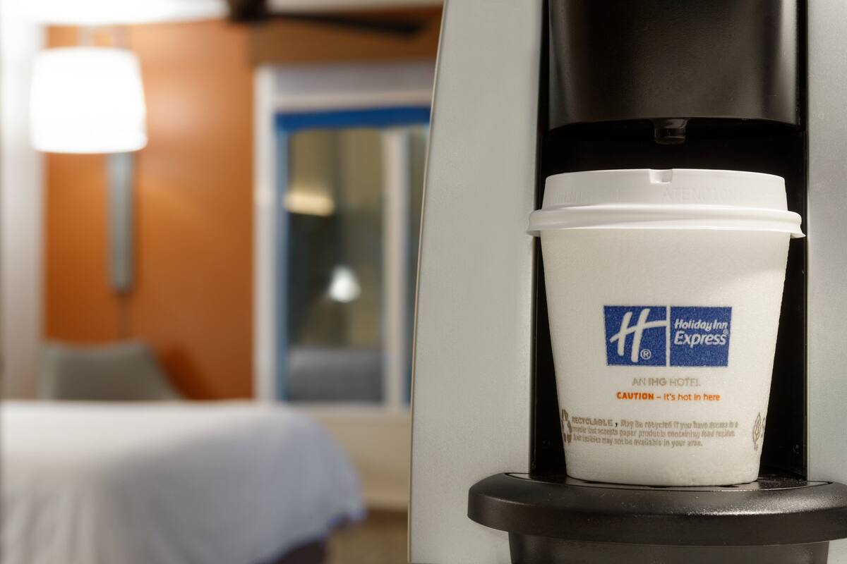 Une tasse à café de la marque Holiday Inn Express, posée sur une machine à café dans une chambre d’hôtel.