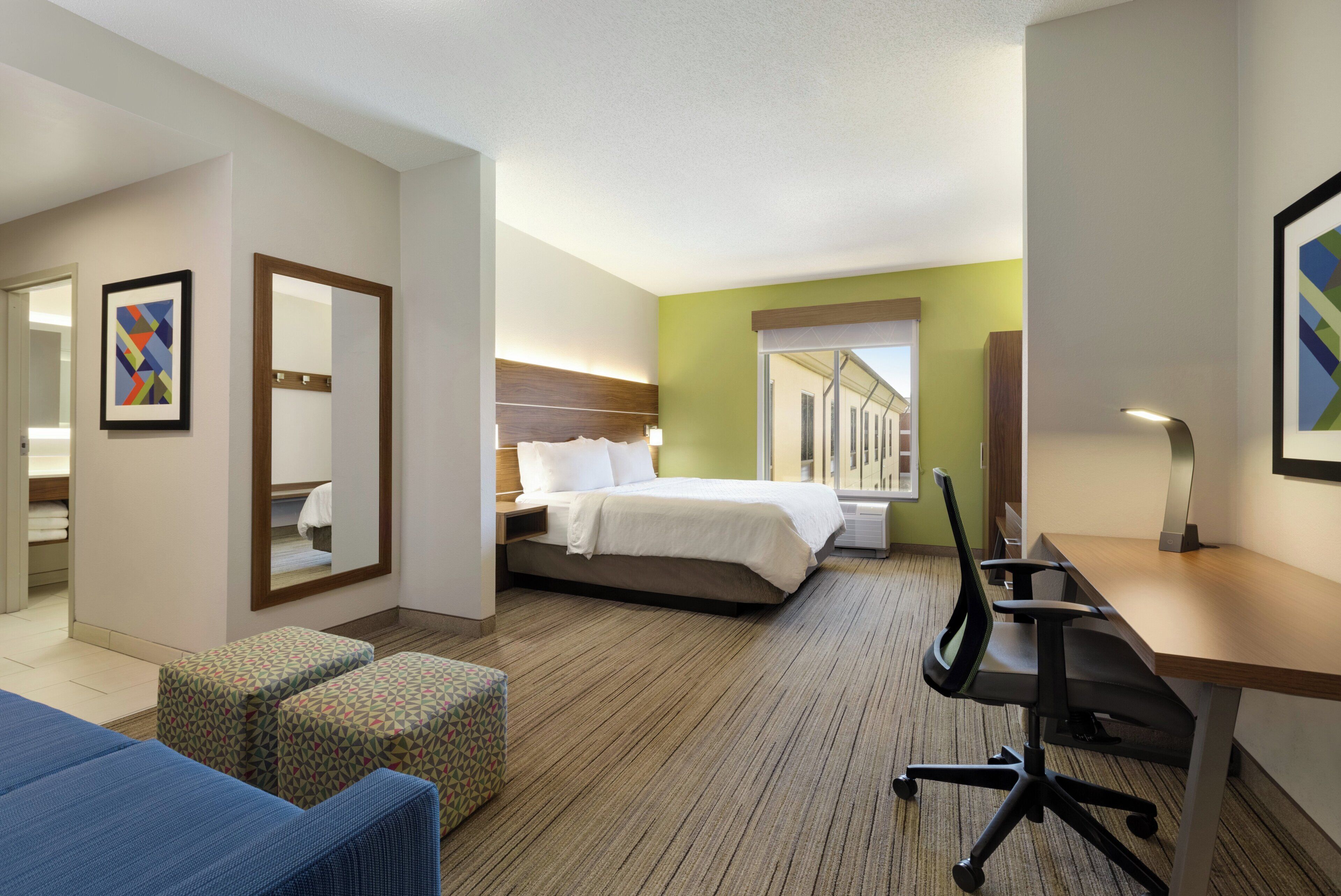 A hotel room with a bed, a desk, a chair, a sofa, and a large window.