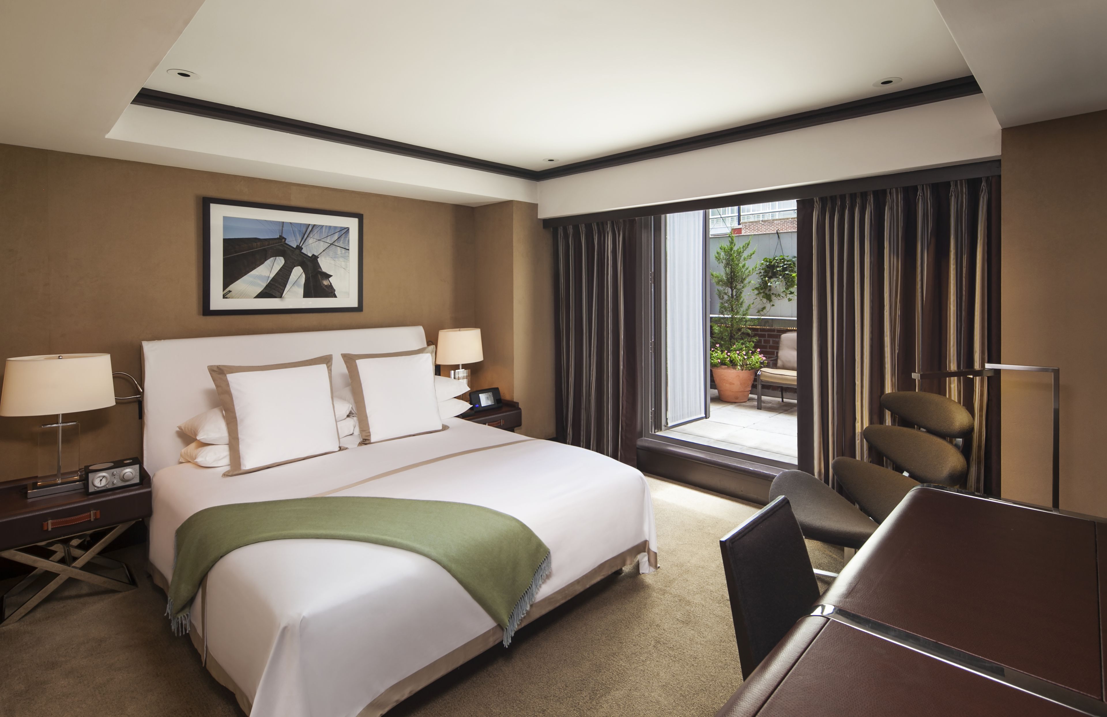 A hotel room with a large bed, a desk with a lamp, a chair, and a view of the outdoors.
