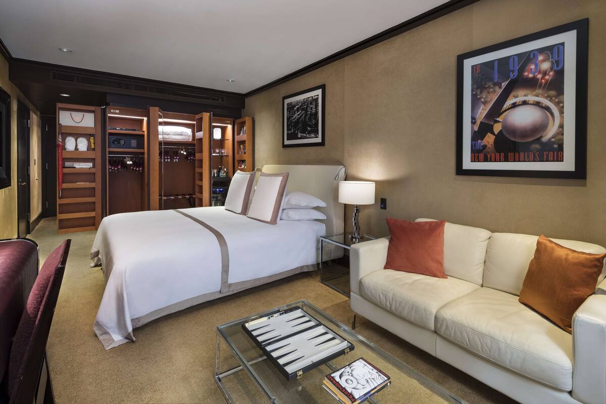 A hotel room with a large bed, a sofa, a glass coffee table, and a wardrobe with a mirror.