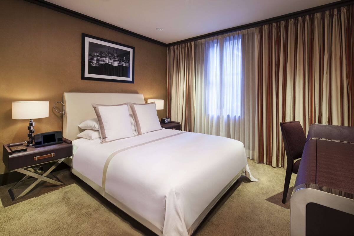 A hotel room with a large bed, two bedside tables, a chair, and a window with curtains.