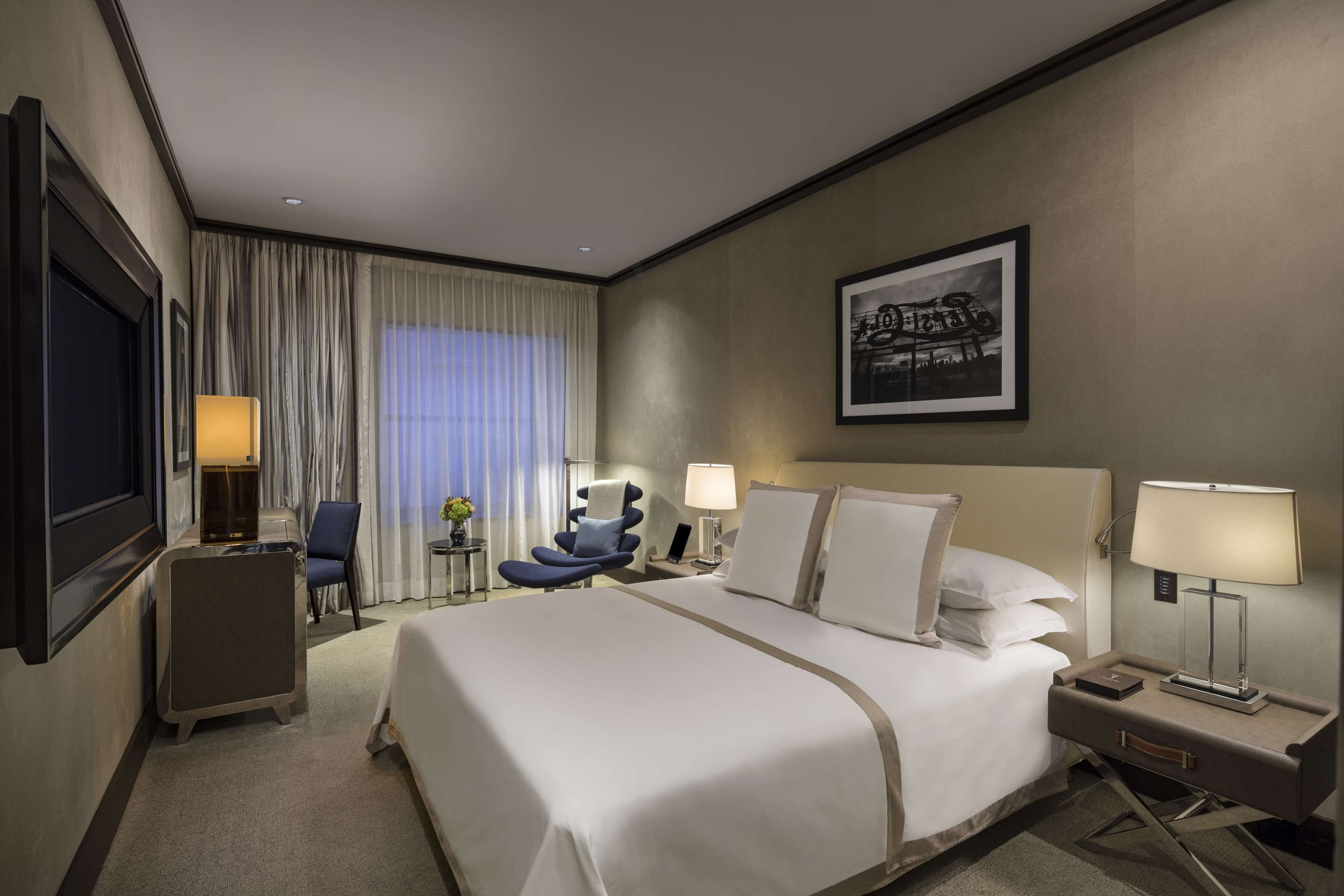 Habitación de hotel con una cama grande, mesitas de noche, un escritorio con una silla, una ventana con cortinas y un cuadro en la pared.