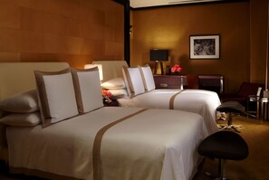 A hotel room with two beds, a desk, a chair, and a lamp.