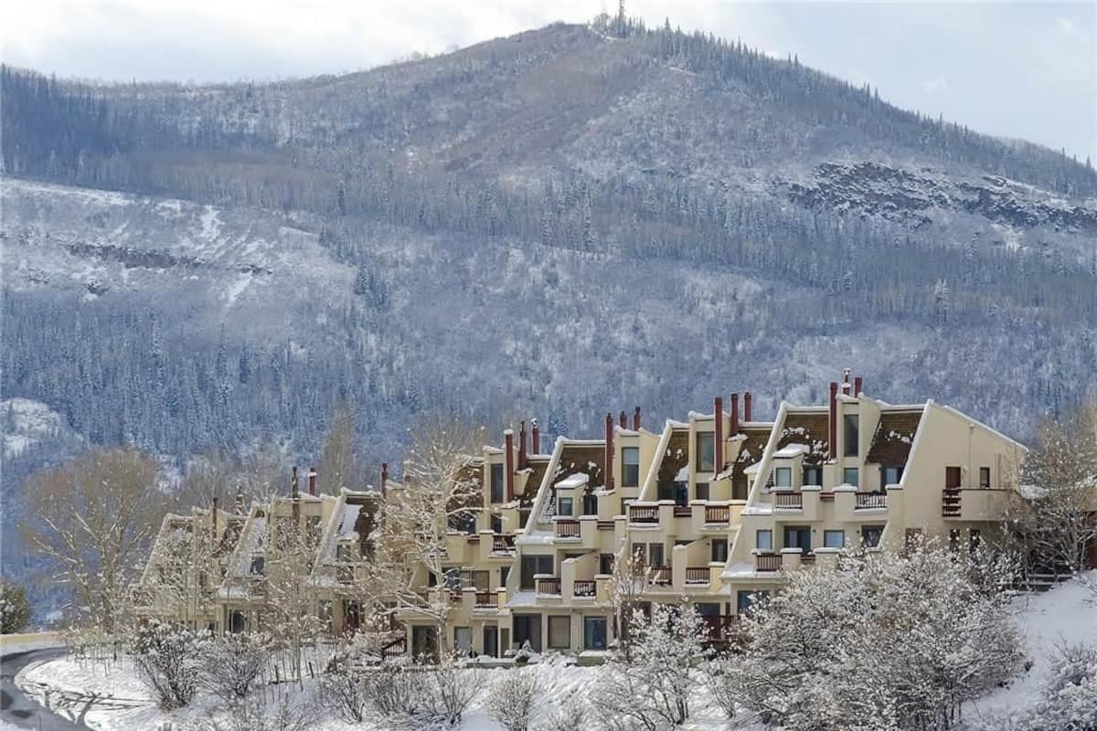 A multi-story hotel with a modern architectural design, featuring balconies and a view of a snow-covered mountain.