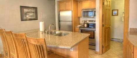 A kitchen with wooden cabinets, a stainless steel refrigerator, a microwave, and a stove. There is a wooden dining table with chairs.
