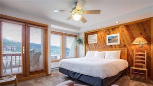A bedroom with a large bed, wooden paneling on the walls, a ceiling fan, and a view through the windows. - Storm Watch Condominiums by Pioneer Ridge Management (Steamboat Springs)