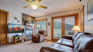A living room with a brown leather couch, a fireplace, a television, and a ceiling fan. - Storm Watch Condominiums by Pioneer Ridge Management (Steamboat Springs)