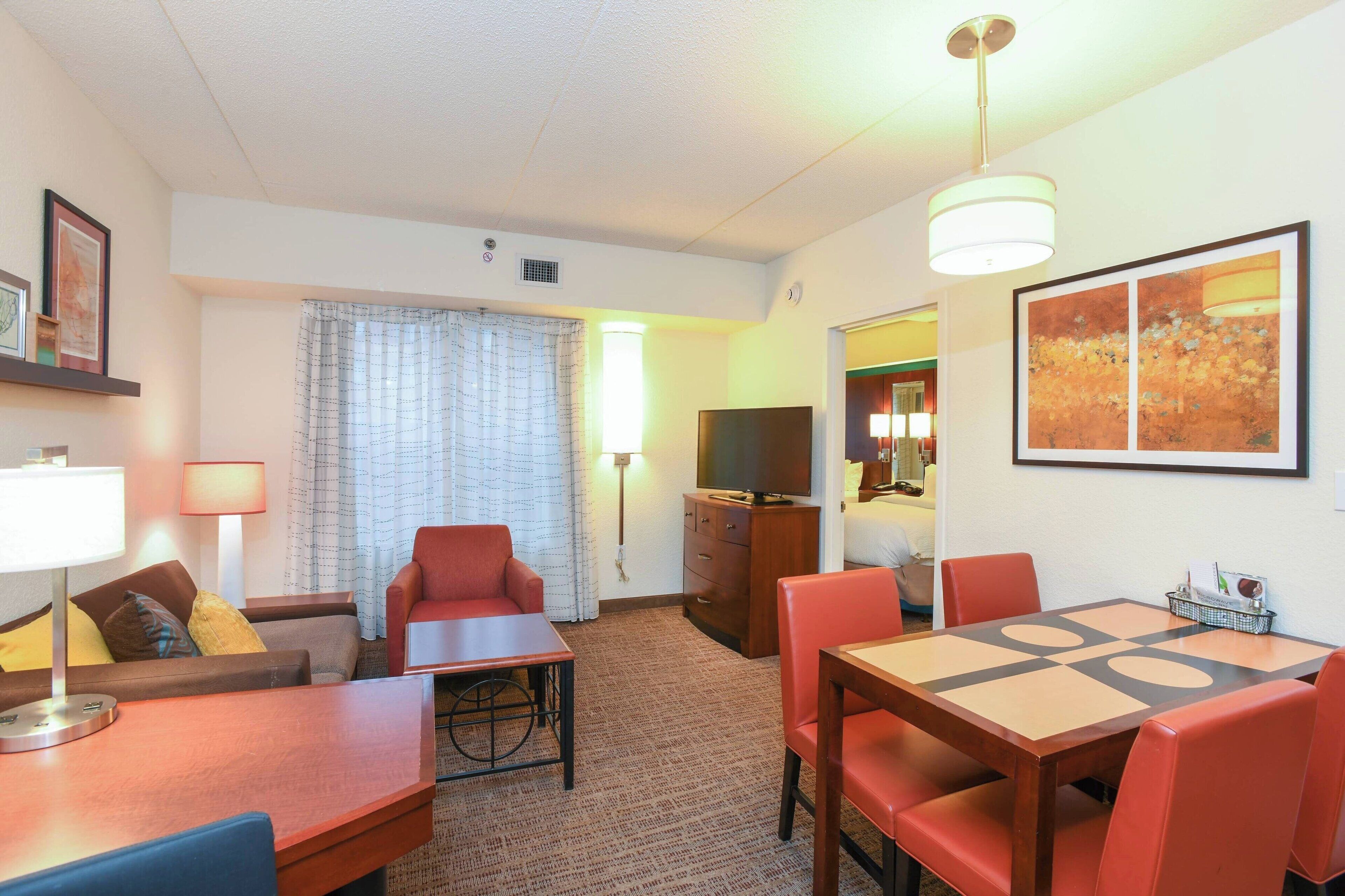 Une chambre d’hôtel avec un canapé, une table à manger avec des chaises, une télévision et un tableau au mur.