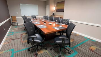A conference room with a long table, multiple chairs, a projector screen, and a carpeted floor.