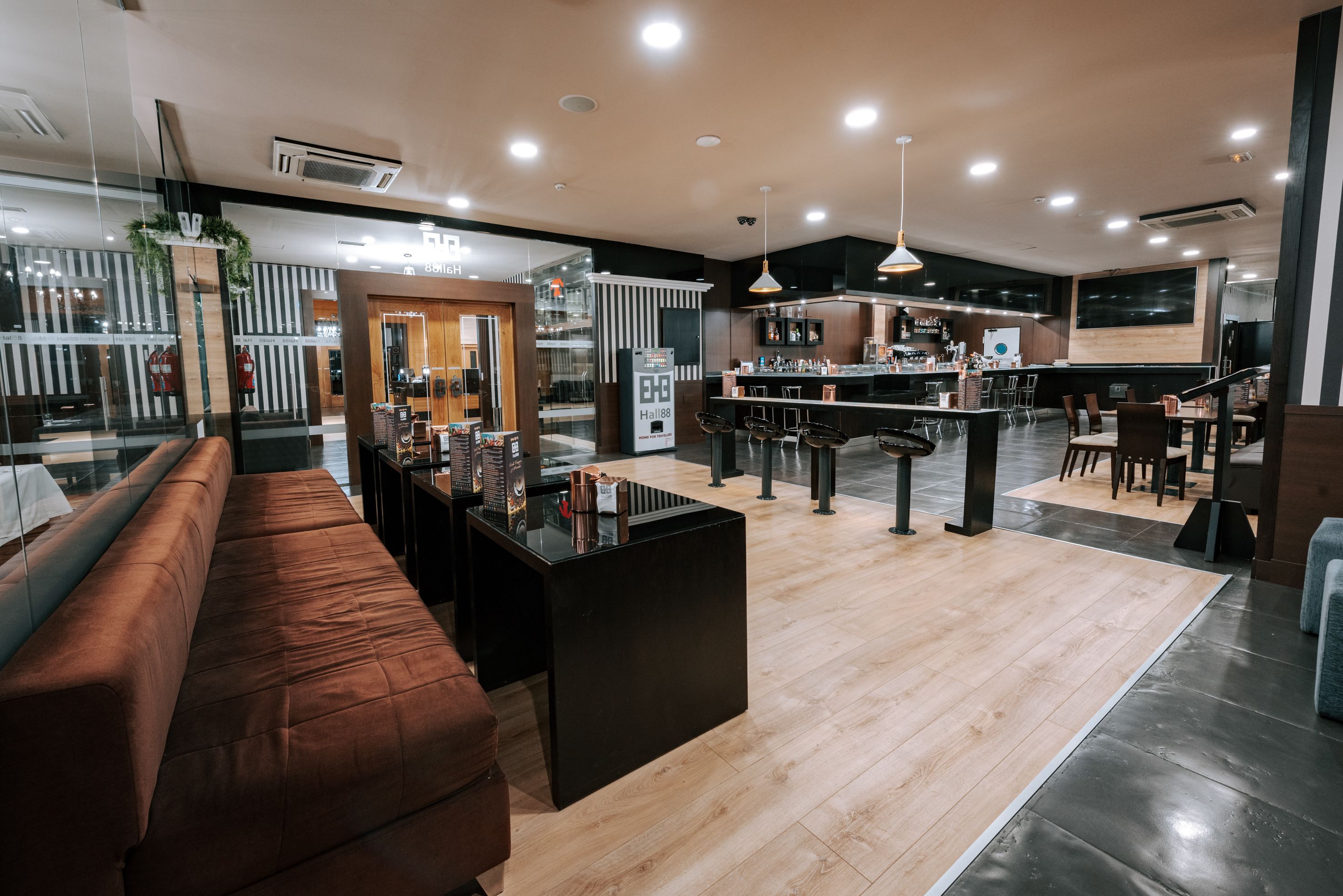 Un hall d’hôtel moderne avec un espace salon, un bar et une cuisine visible au fond.
