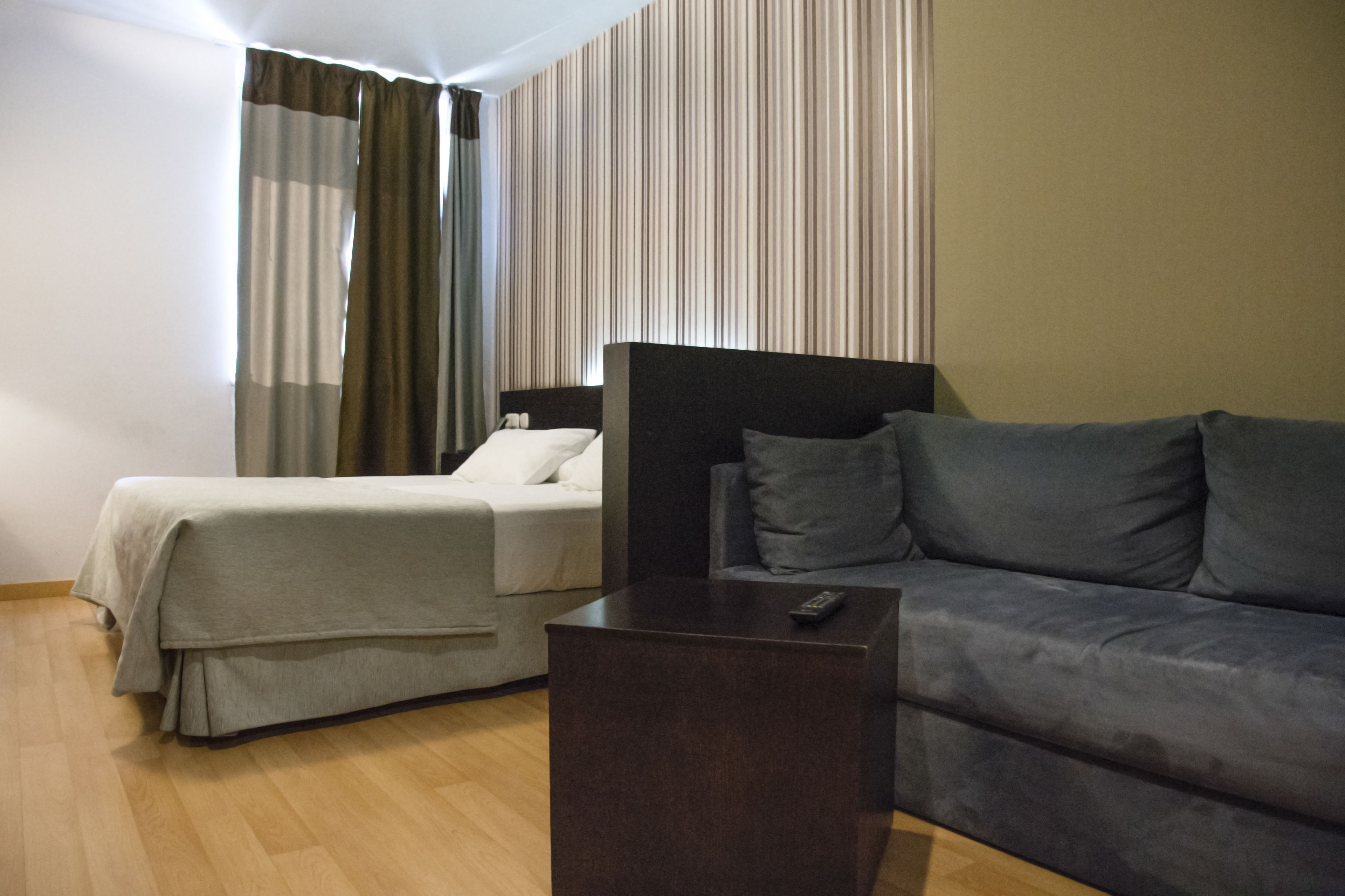 A hotel room with a bed, a sofa, a nightstand, and a window with curtains.