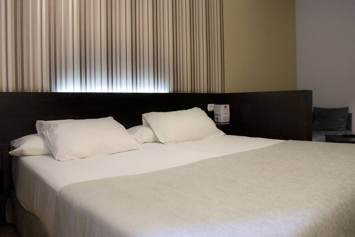 Habitación de hotel con una cama grande, cabecero, mesita de noche y teléfono instalado en la pared.