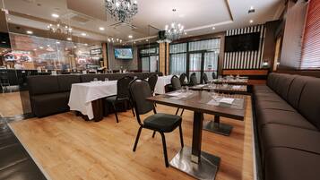 Un restaurante moderno con suelo de madera, un área de comedor central con mesas y sillas, y una pantalla grande que muestra un mapa.