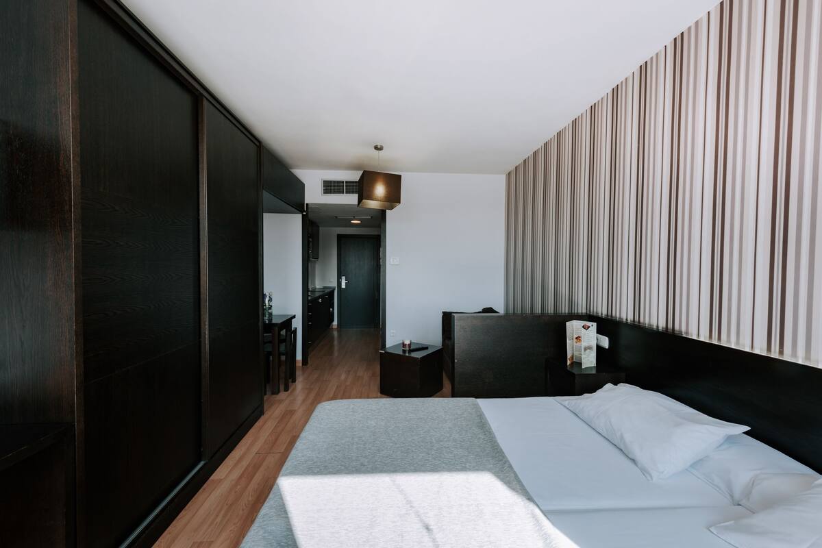 Una habitación de hotel moderna con una cama grande, una mesita de noche y vistas al pasillo.