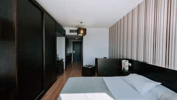 A modern hotel room with a large bed, a bedside table, a nightstand, and a view of the hallway.
