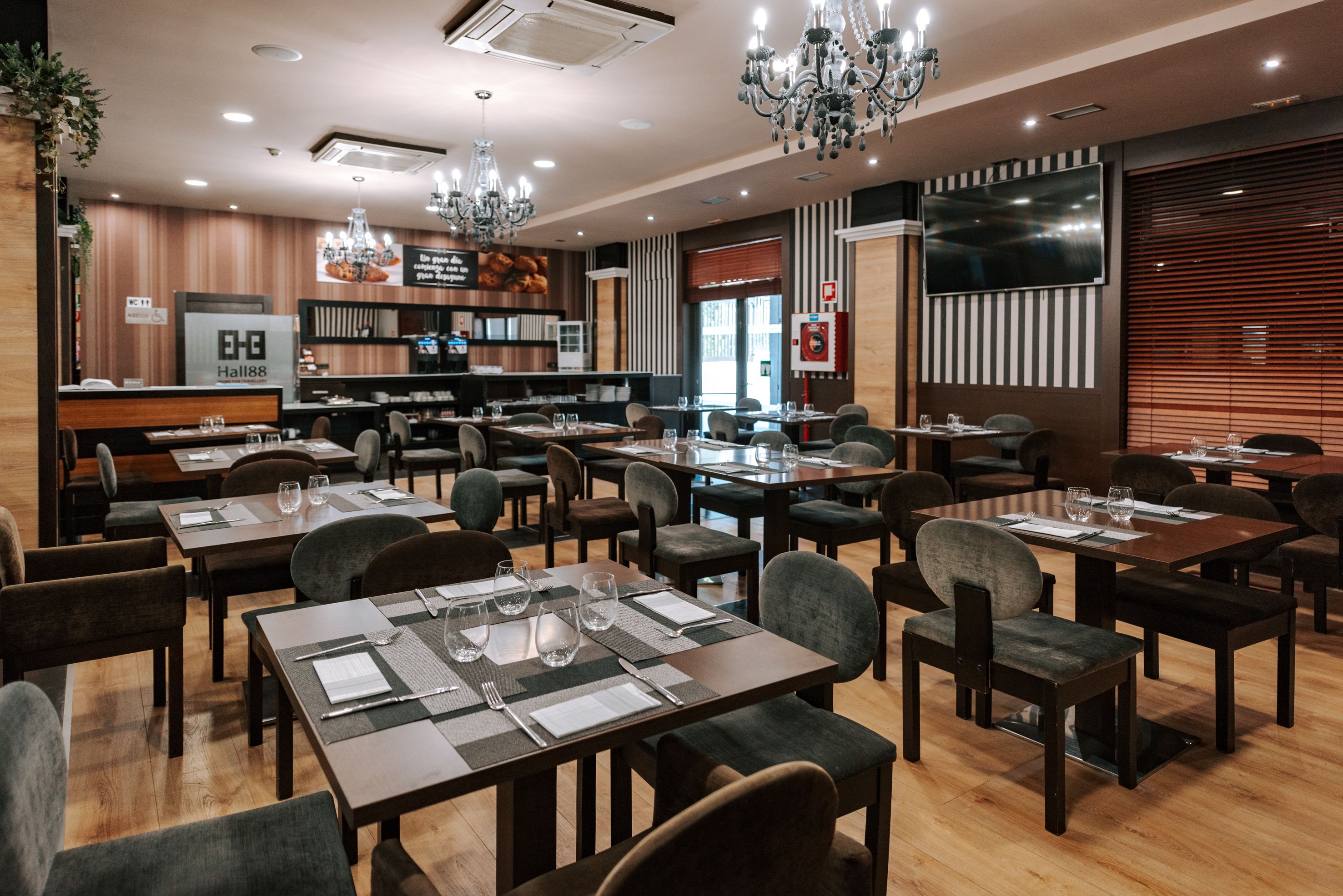 A restaurant with multiple tables and chairs, a chandelier, and a television on the wall.