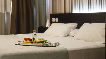 Una cama bien hecha con ropa blanca, una bandeja con frutas y una botella, y una mesita de noche con una lámpara.