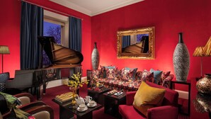 A red-walled room with a grand piano, a sofa set, and a large mirror. - Rocpool Reserve (Inverness)