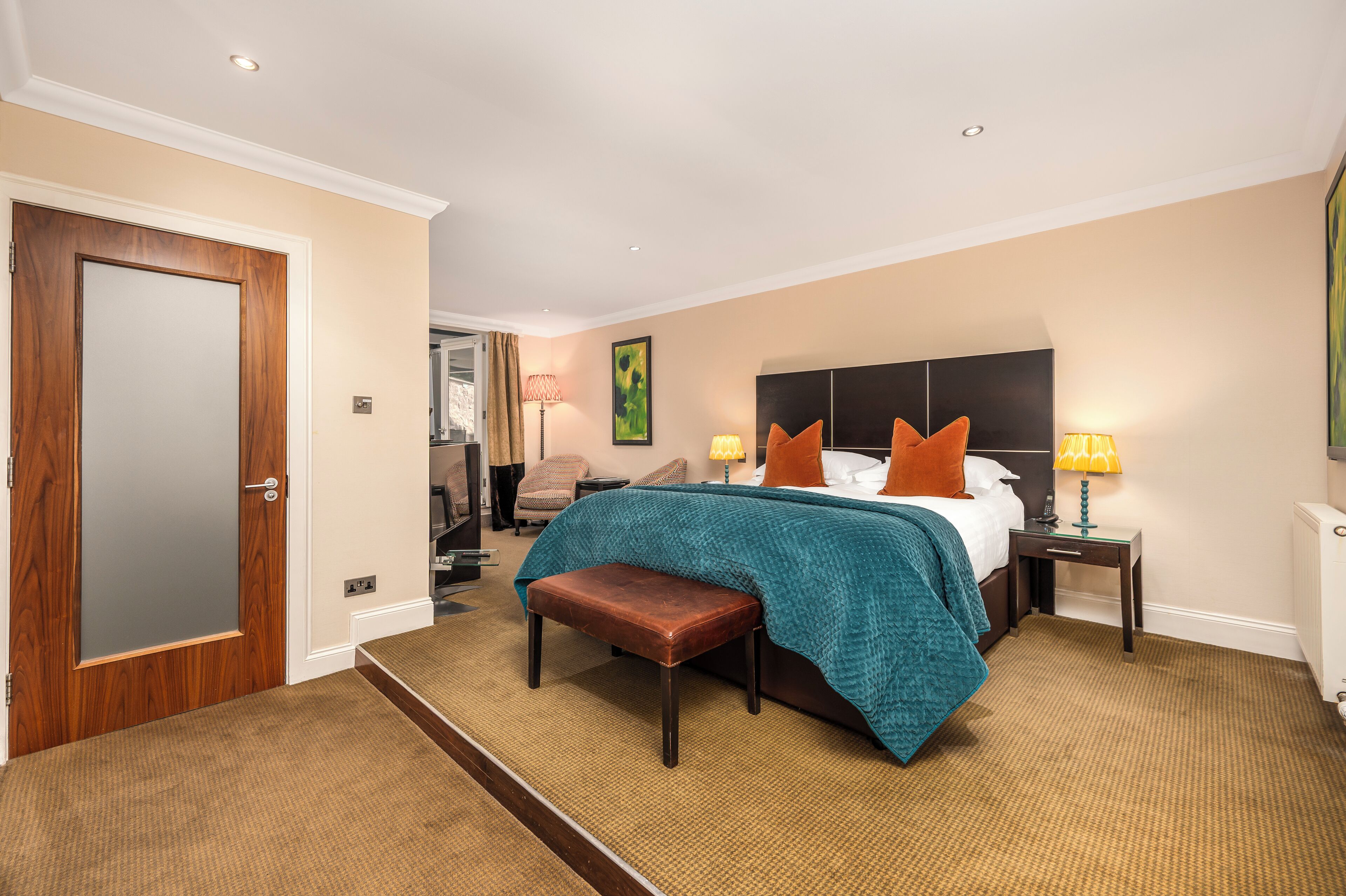 A hotel room with a large bed, two bedside tables, a bench, and a view of the city through the window.
