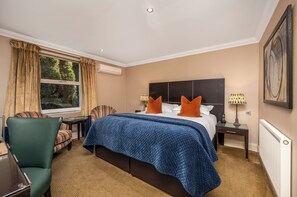 A hotel room with a large bed, a desk, a chair, and a window with curtains.