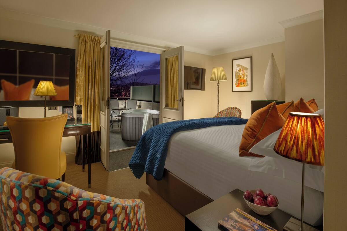 A hotel room with a bed, a desk, a chair, a TV, and a view of the outside.