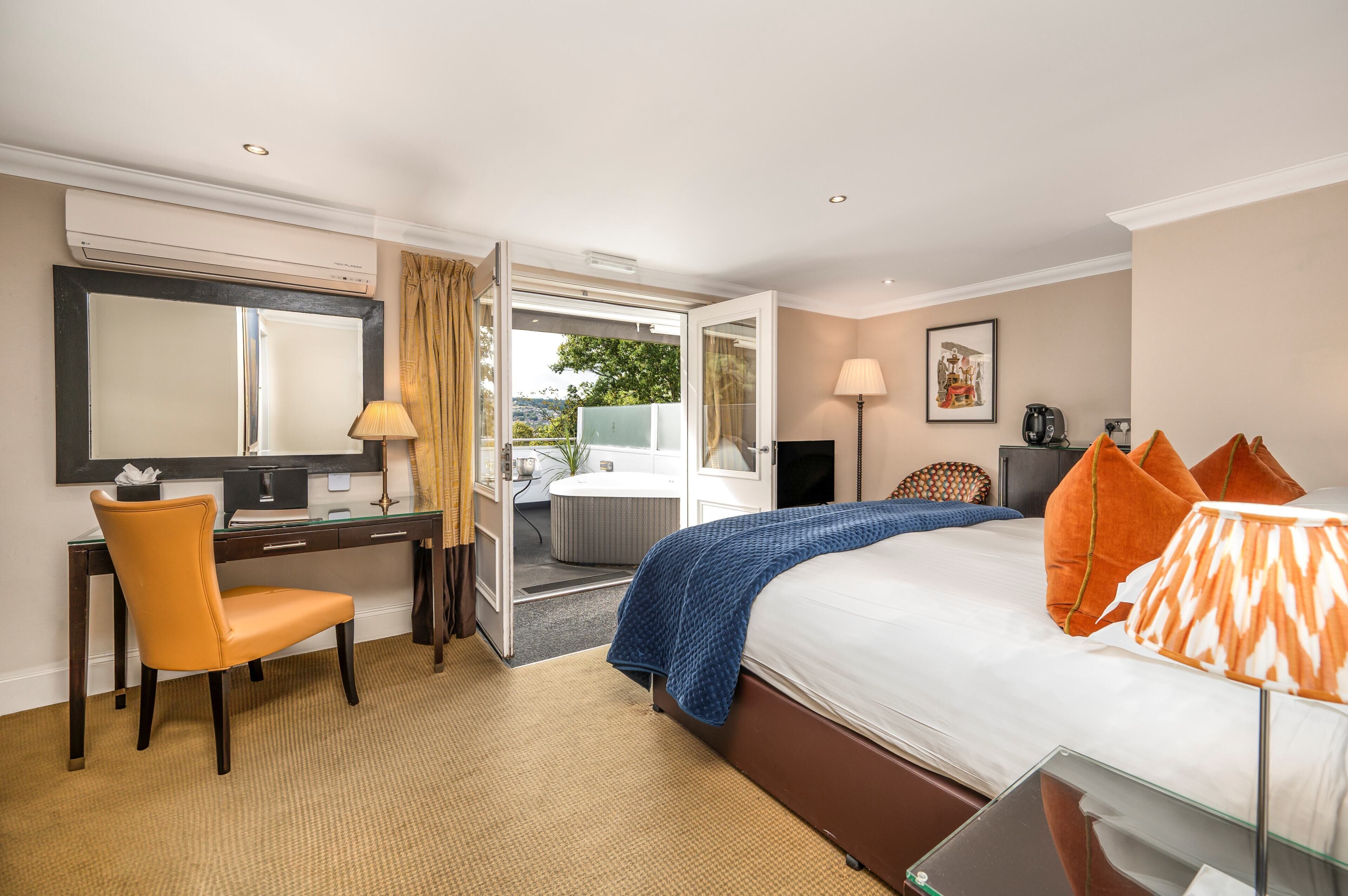 A hotel room with a bed, a desk, a chair, a TV, and a bathroom visible through an open door.
