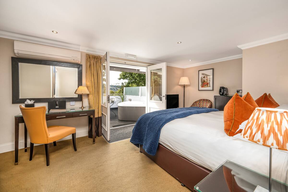 A hotel room with a bed, a desk, a chair, a TV, a lamp, and a view of the outdoors.