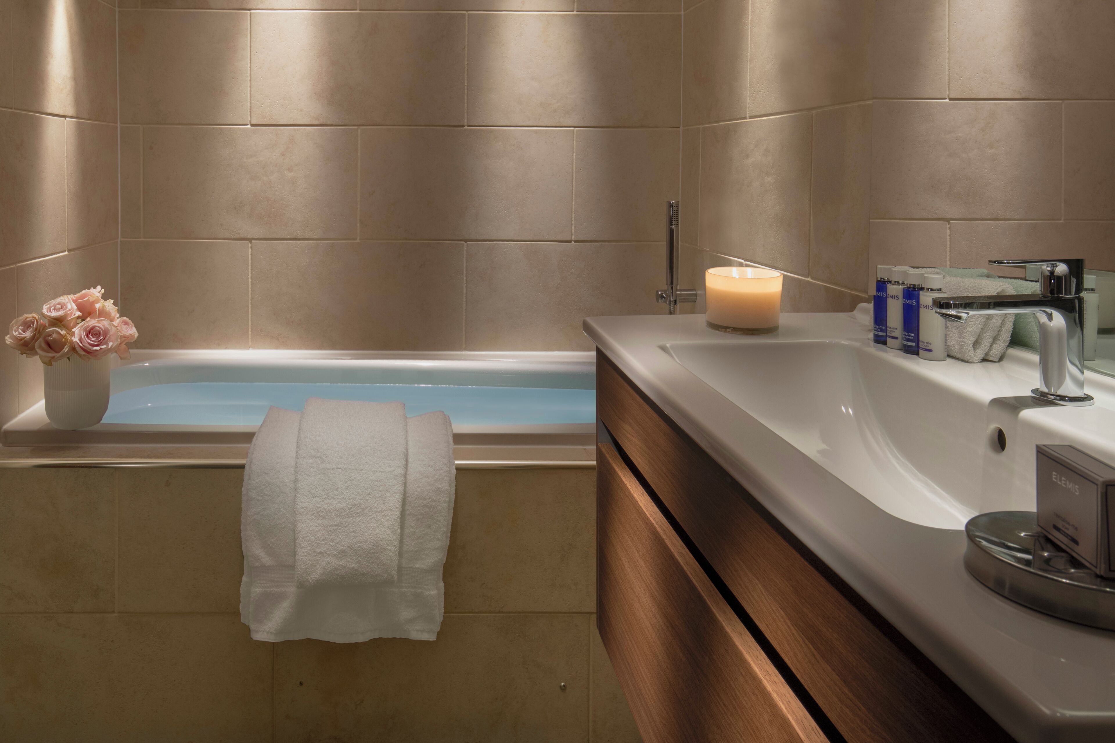 Un baño con bañera, tocador con espejo, una toalla y una vela.