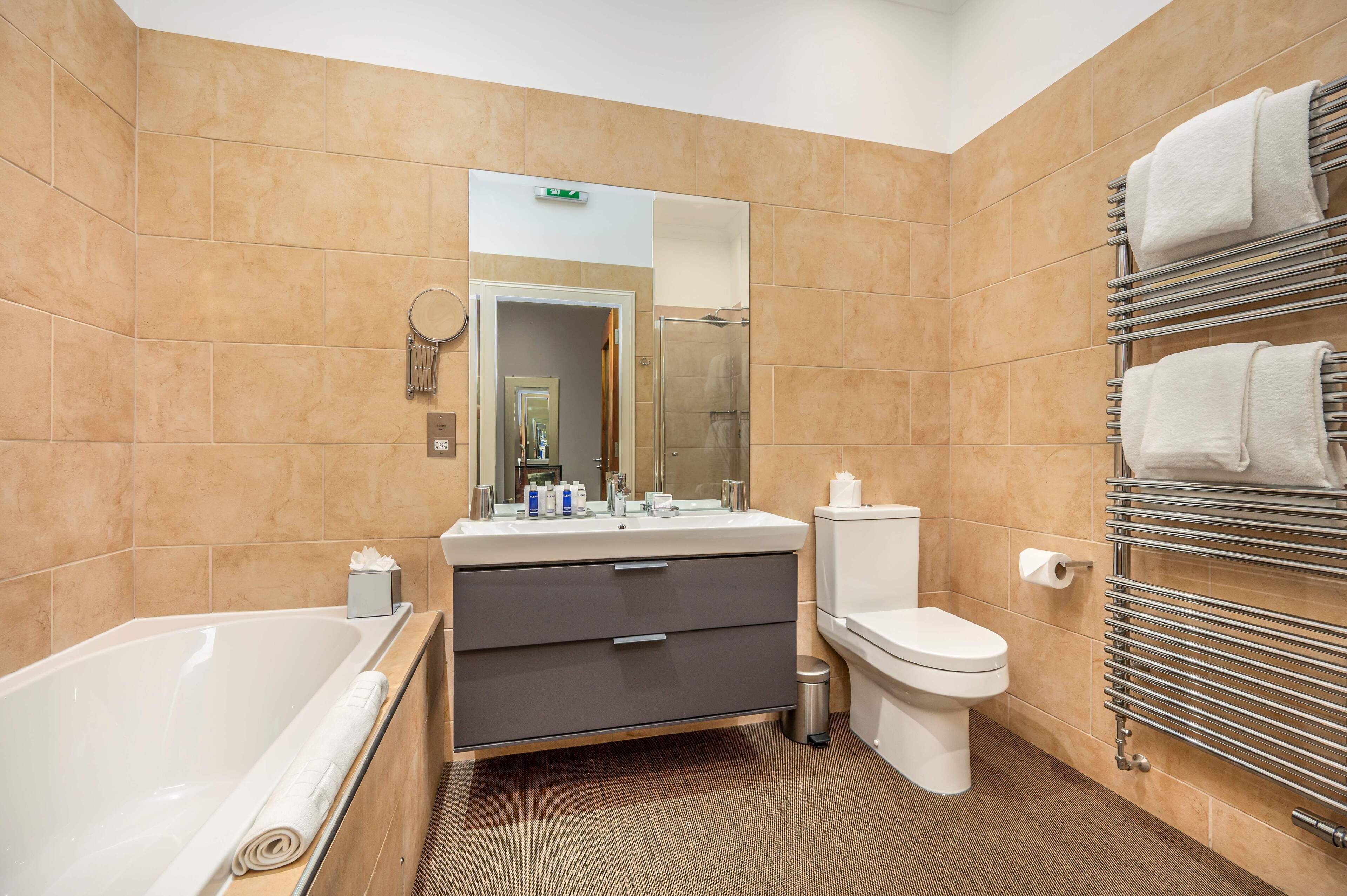 A modern bathroom with a bathtub, toilet, vanity, and towel rack.