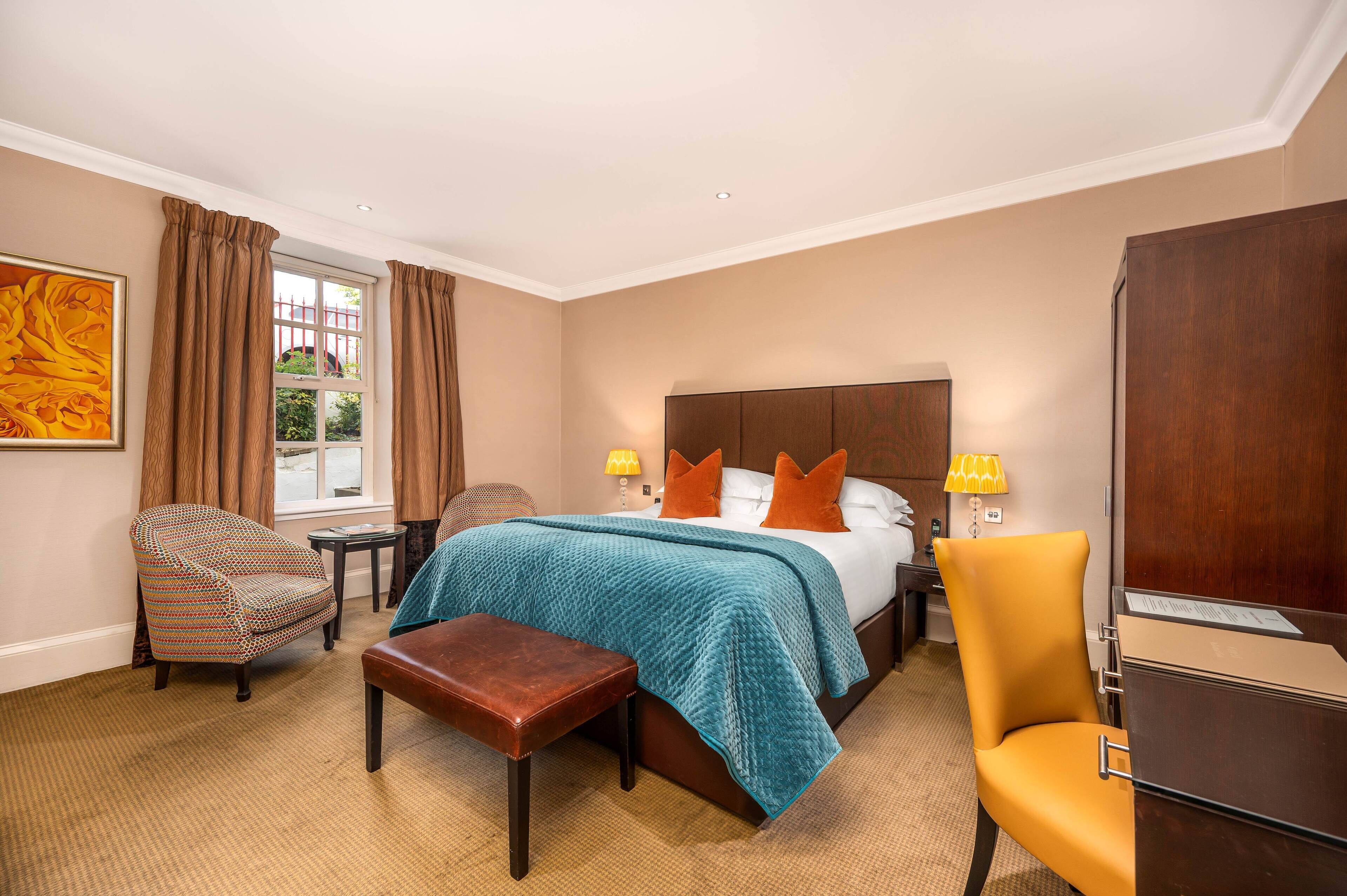 A hotel room with a large bed, two side tables, a chair, a desk, and a window with curtains.