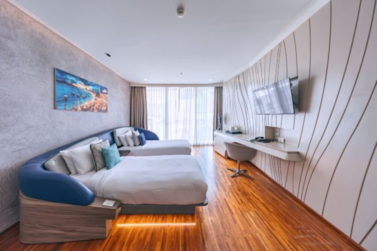 A modern hotel room with a curved bed, a flat-screen TV mounted on the wall, and a wooden floor.